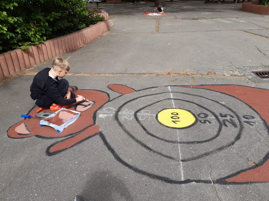 Schüler sitzt auf dem Schulhof und malt Hüpfspiel auf